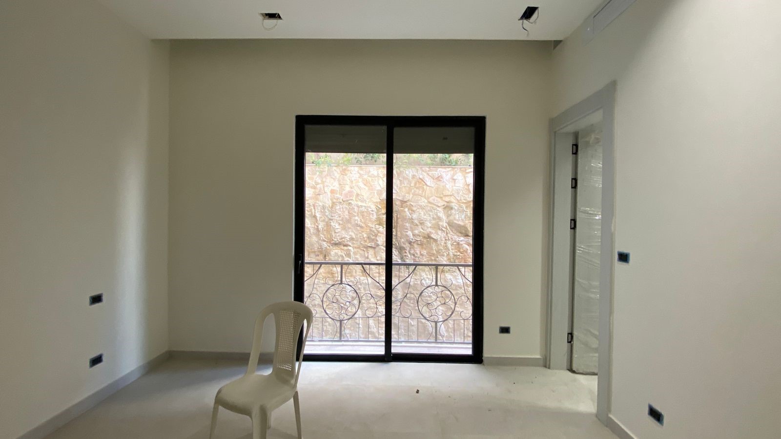 ab8af77c-e749-4f7d-ae4a-dfb1c9192cfc Empty, lightly finished room with a sliding glass door to a balcony and a white plastic chair in the foreground.