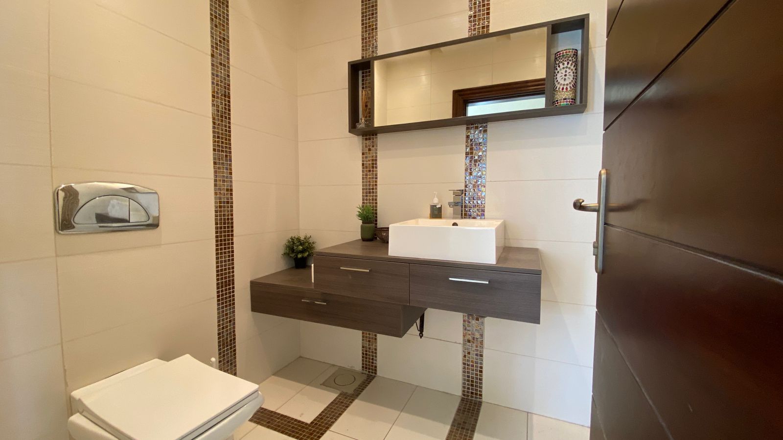 adb8a50d-873a-4734-b152-d20e5347f760 Modern bathroom with a wall-mounted dark wood vanity, white rectangular sink, and vertical mosaic tile accents.