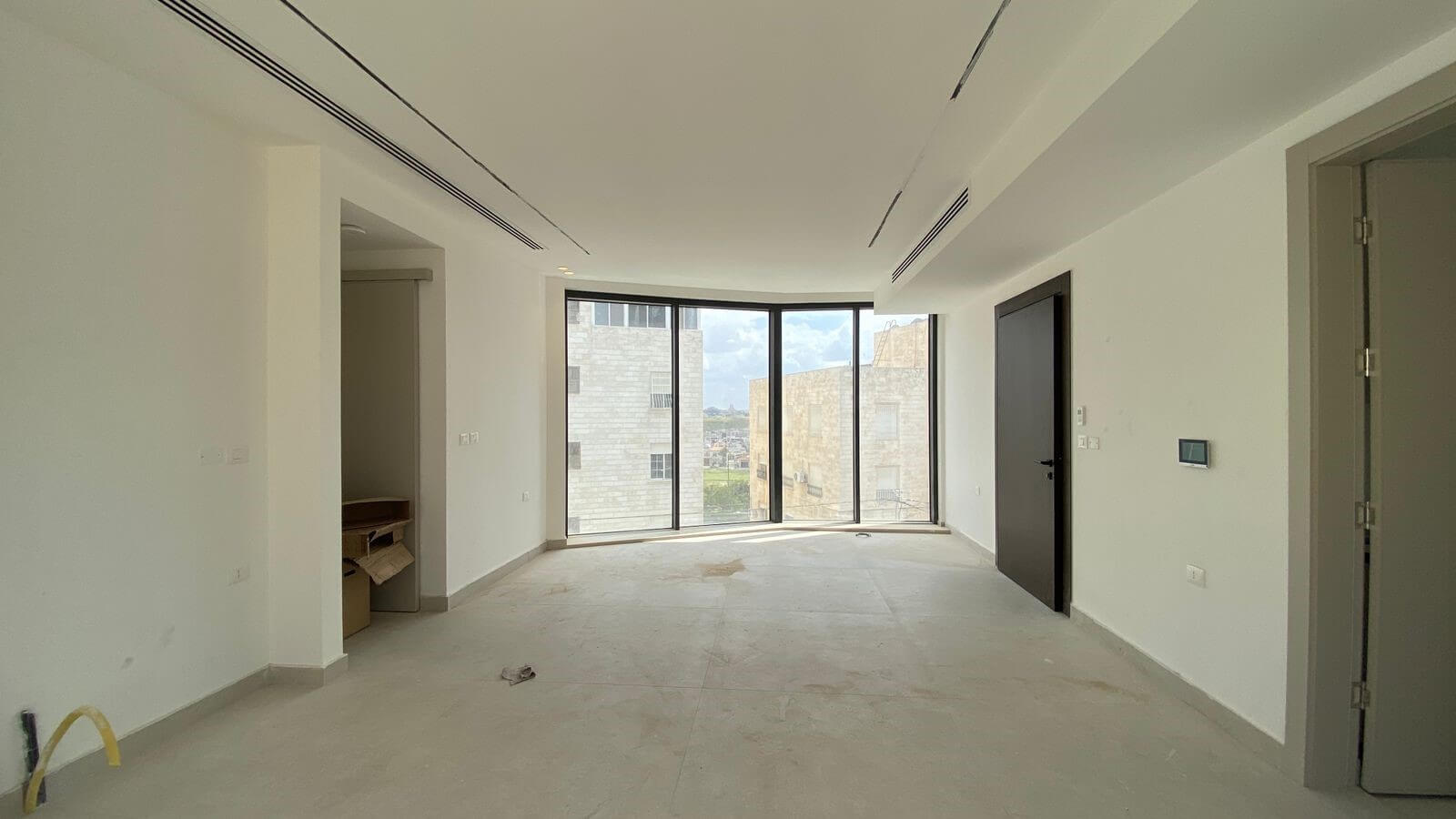 b07e2fda-1ac3-4bf9-bb61-dc13f866a331 Unfurnished white living room with large curved floor-to-ceiling windows and city view, neutral tiled floor, doorway on the right.