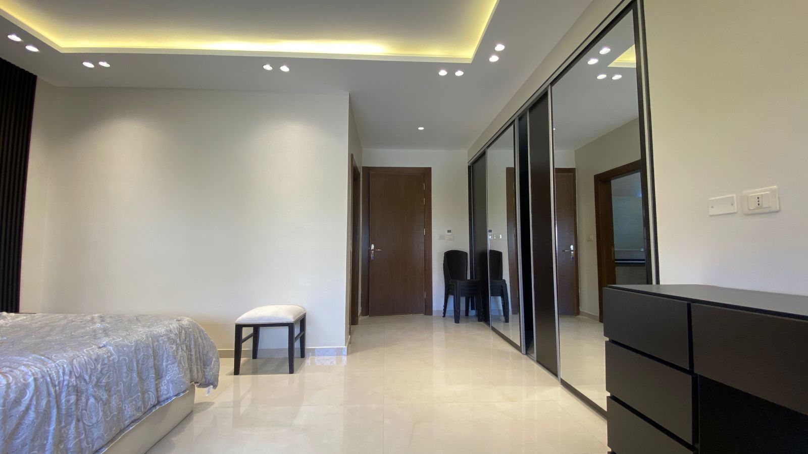 b4de16b2-66ee-4341-aab3-9d6739cbc8f7 Modern bedroom with a low bed on the left, light gray bedding, and a small white stool near the wall