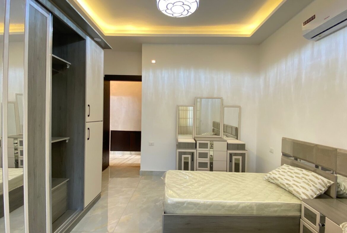 Modern bedroom with a low-profile bed, gray headboard, matching nightstands, and a dresser with mirrors.