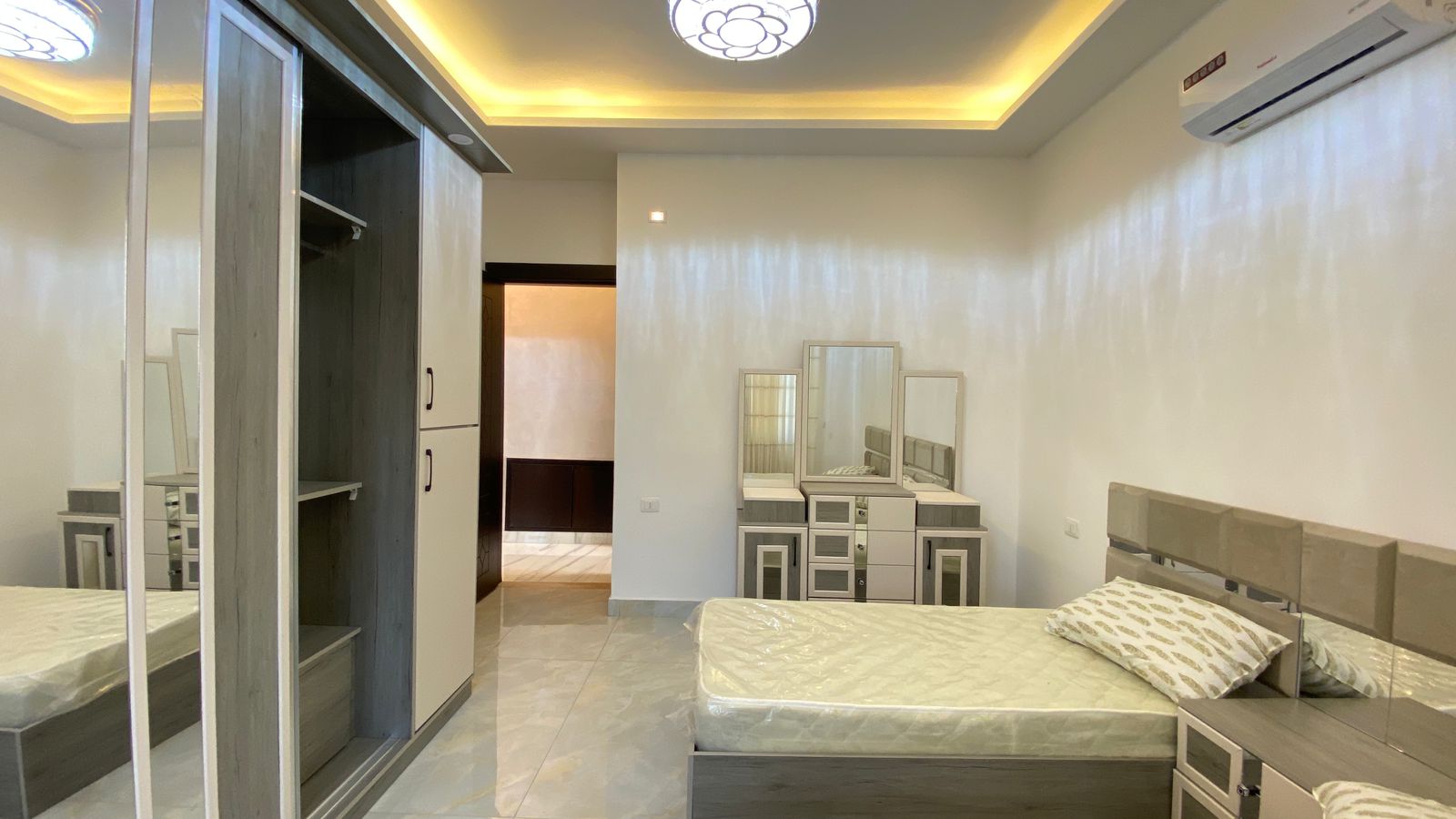 Modern bedroom with a low-profile bed, gray headboard, matching nightstands, and a dresser with mirrors.