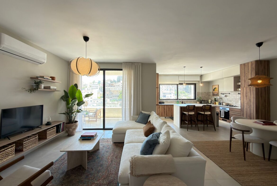 Open-plan living room and kitchen with a white sofa, wooden accents, and a balcony view. (informative)