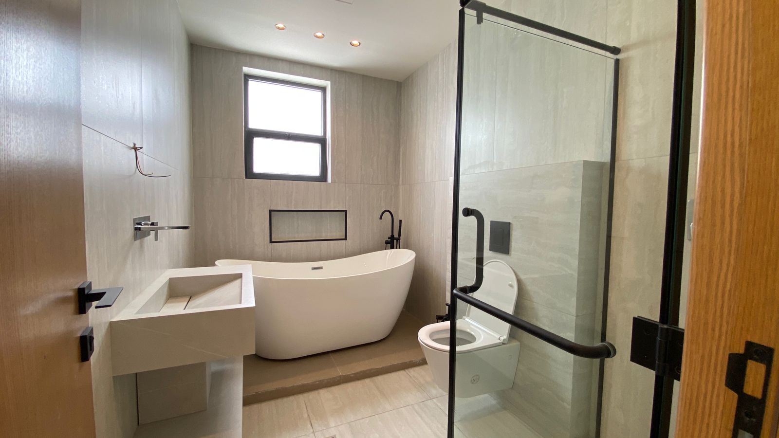 b89b9674-5920-4656-90cf-29d986bb7c61 Modern bathroom with a white freestanding tub by a window, rectangular sink, and glass-enclosed shower.