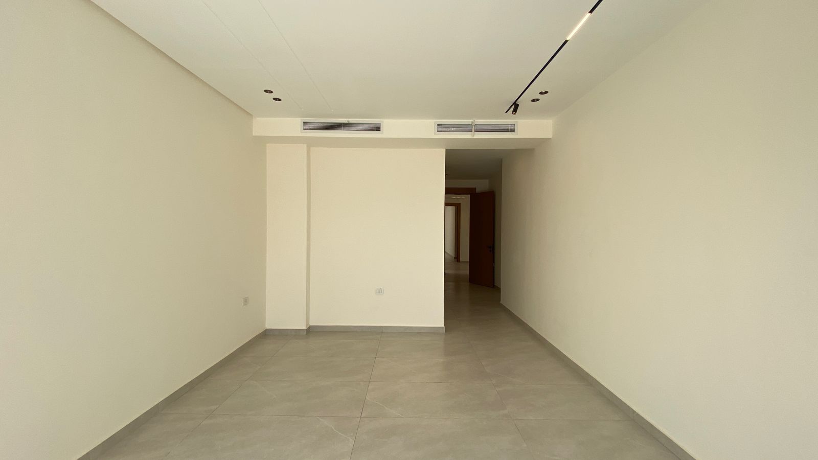 b9b96c0c-1774-4edd-b3d0-f8212afe9a08 Empty white-walled hallway with a gray tile floor and recessed ceiling lights up top.