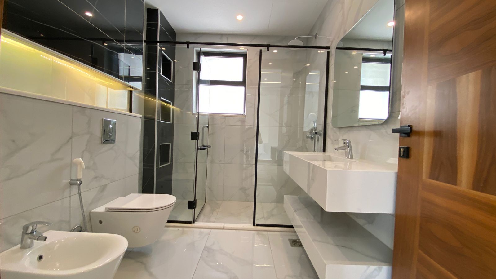 bb143d10-62e4-4649-9ee4-a5193237e9bf Modern marble bathroom with glass shower enclosure, wall-mounted toilet and bidet, and a floating white sink.