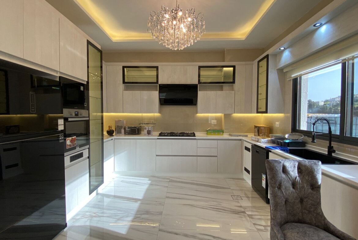 Bright contemporary kitchen with white cabinets, marble floor, and a crystal chandelier centerpiece.