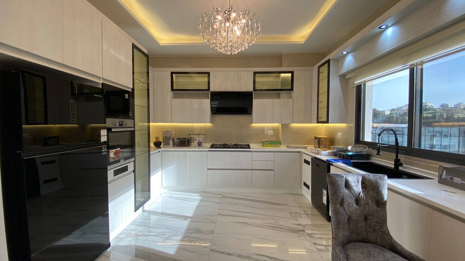 Bright contemporary kitchen with white cabinets, marble floor, and a crystal chandelier centerpiece.