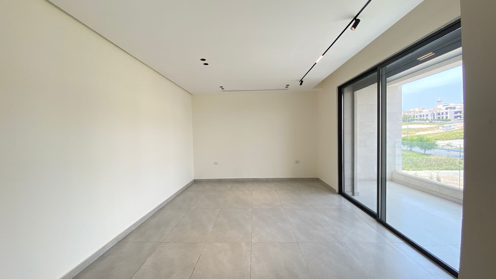 c9701317-c391-46f5-9ea2-14364d3f7151 Empty modern room with gray floor tiles and a large sliding glass door opening to a balcony, flooded with daylight.
