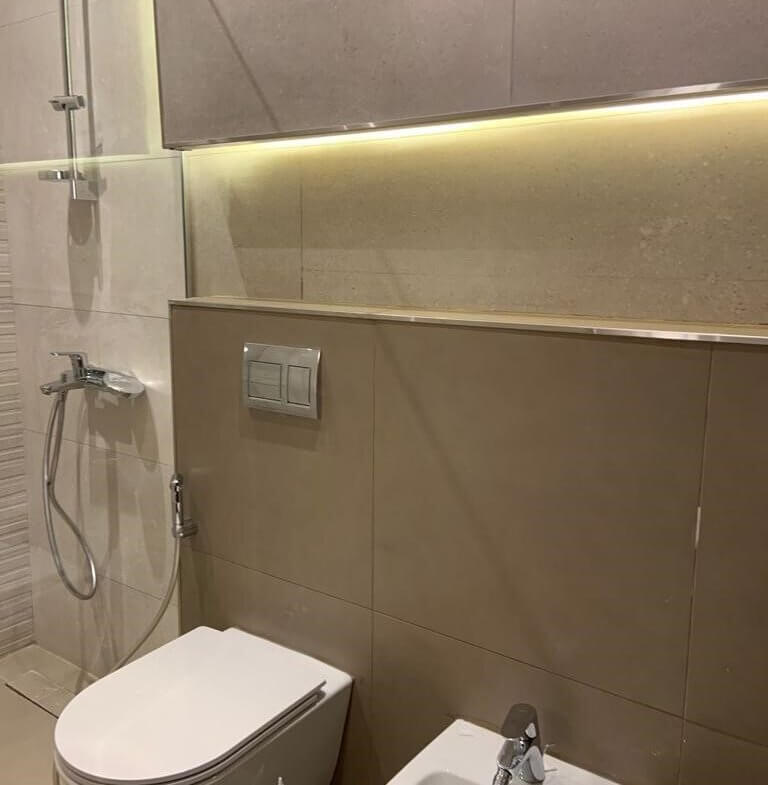 Modern bathroom with wall-mounted toilet, bidet, and glass shower enclosure under warm LED lighting