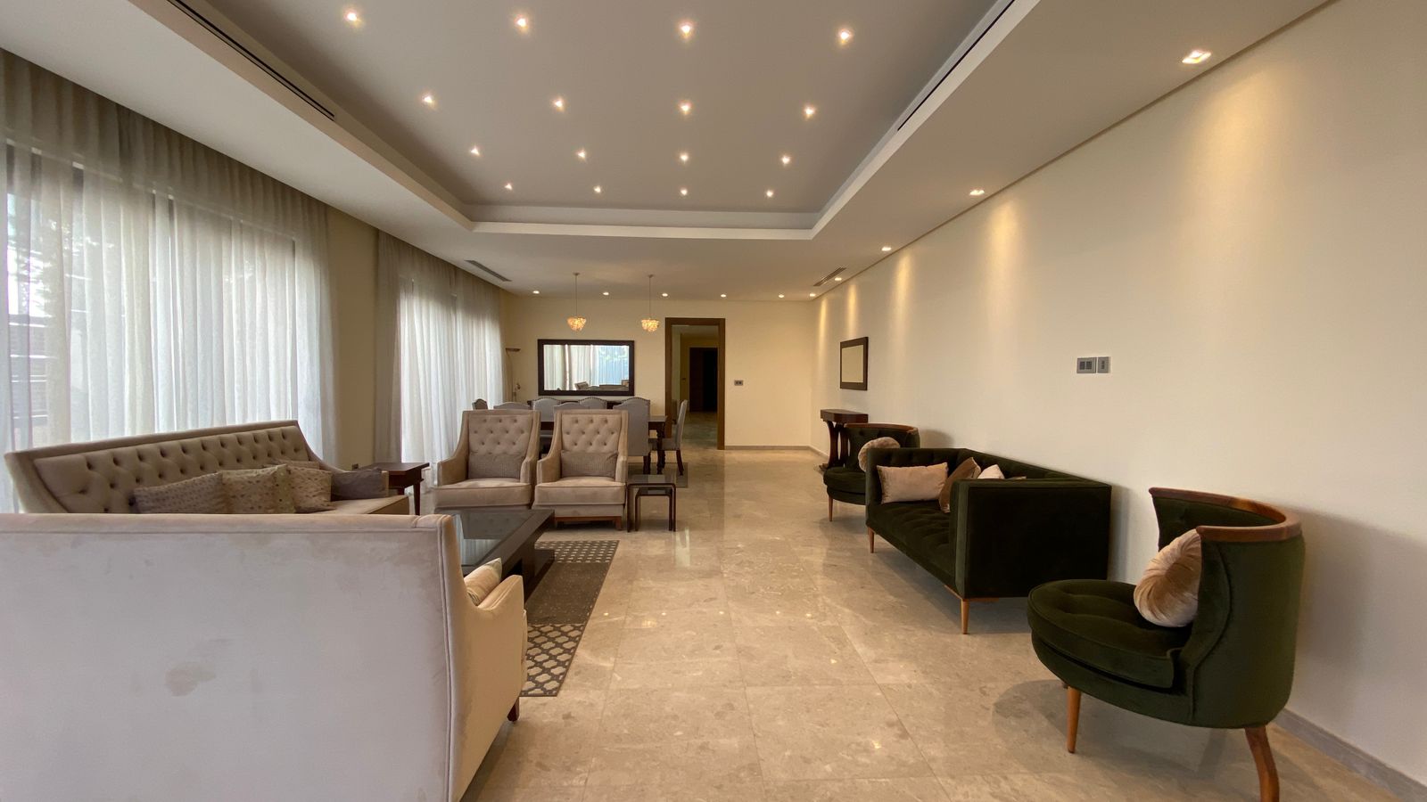 c9ce3c9d-5a3f-46cf-8e58-d1298d49f4a4 Spacious hotel lounge with beige sofas, tufted chairs, and marble floor under recessed ceiling lights.