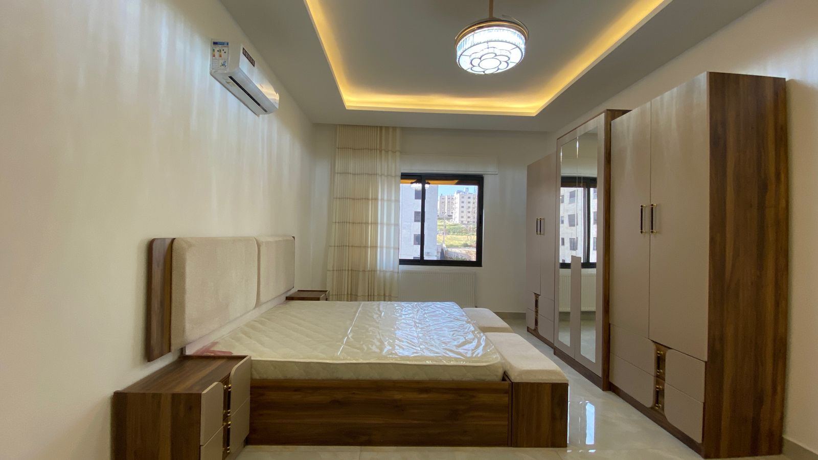 Modern bedroom with a low wooden bed, beige upholstered headboard, and matching nightstands, plus a large mirrored wardrobe.