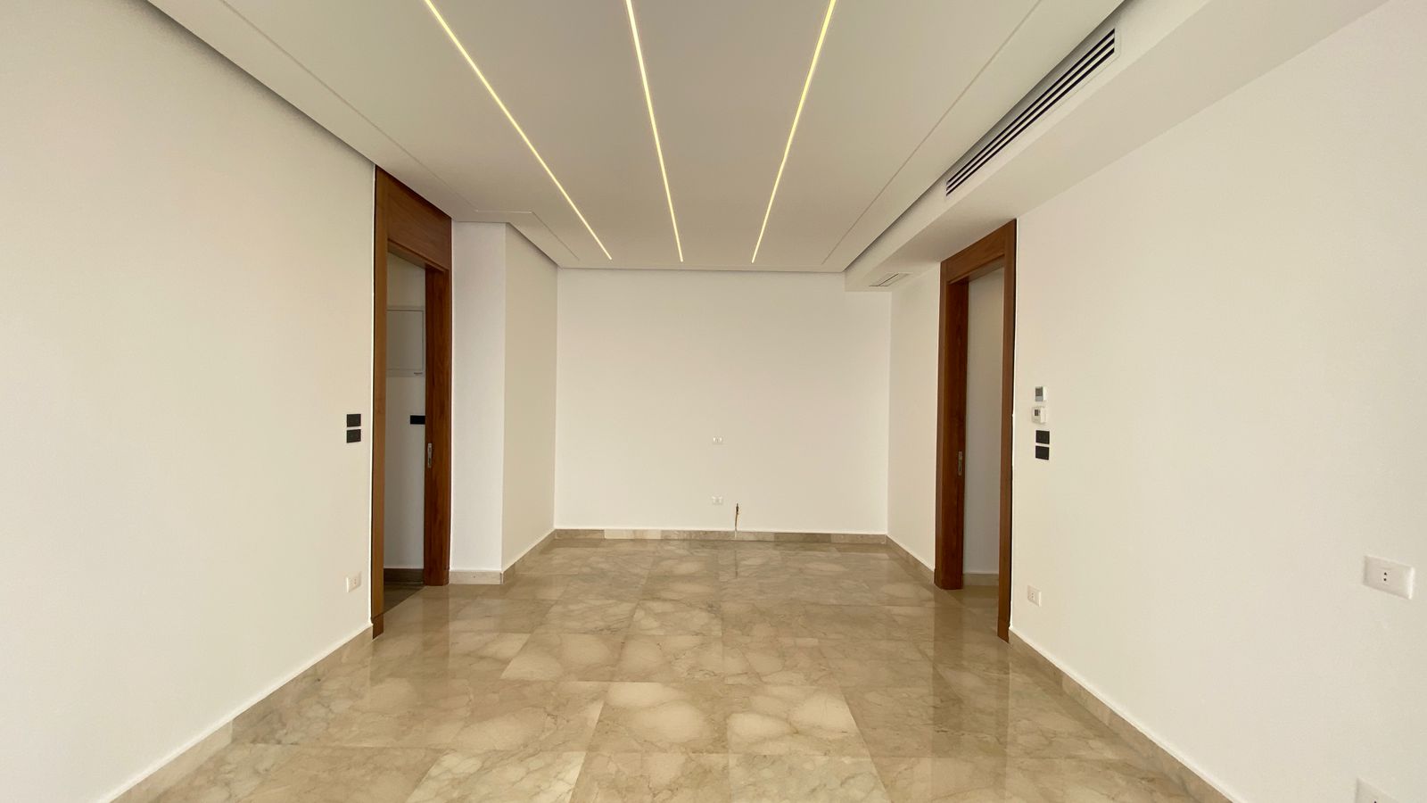 d45a77c4-bc8d-4016-9bde-57dcc2f04727 Empty modern room with white walls, glossy marble floor, and linear recessed ceiling lights.