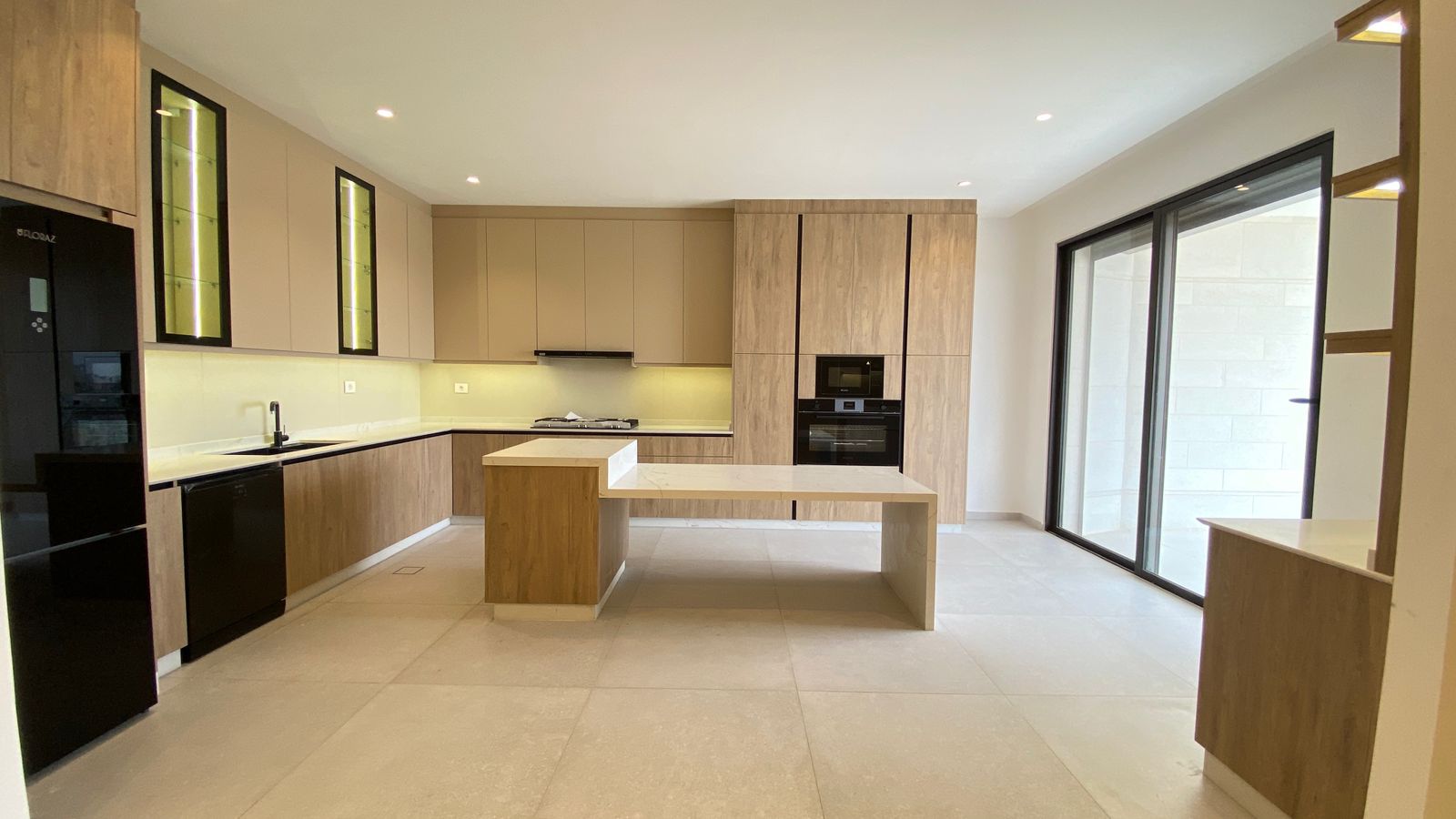 d5ca3207-d2e9-4615-9aec-e6acebc30bfa Modern open-concept kitchen with light wood cabinets, a central island, and built-in double ovens near large glass sliding doors to an outdoor area.