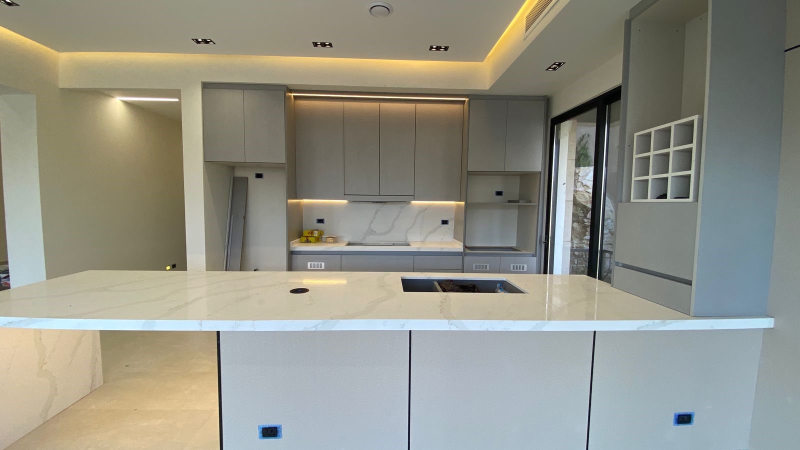 d5d8cbf1-7937-43ec-b35f-6ba56a53e109 Modern, minimalist kitchen with a large marble island, gray cabinets, and under-cabinet lighting above a marble backsplash.