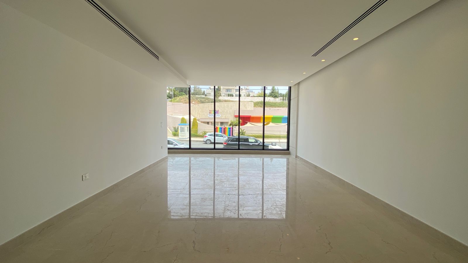d6a8d548-c9e3-4408-811e-e97afb969e05 Empty modern showroom with glossy marble floor, white walls, recessed ceiling lights, and large front windows overlooking the street.