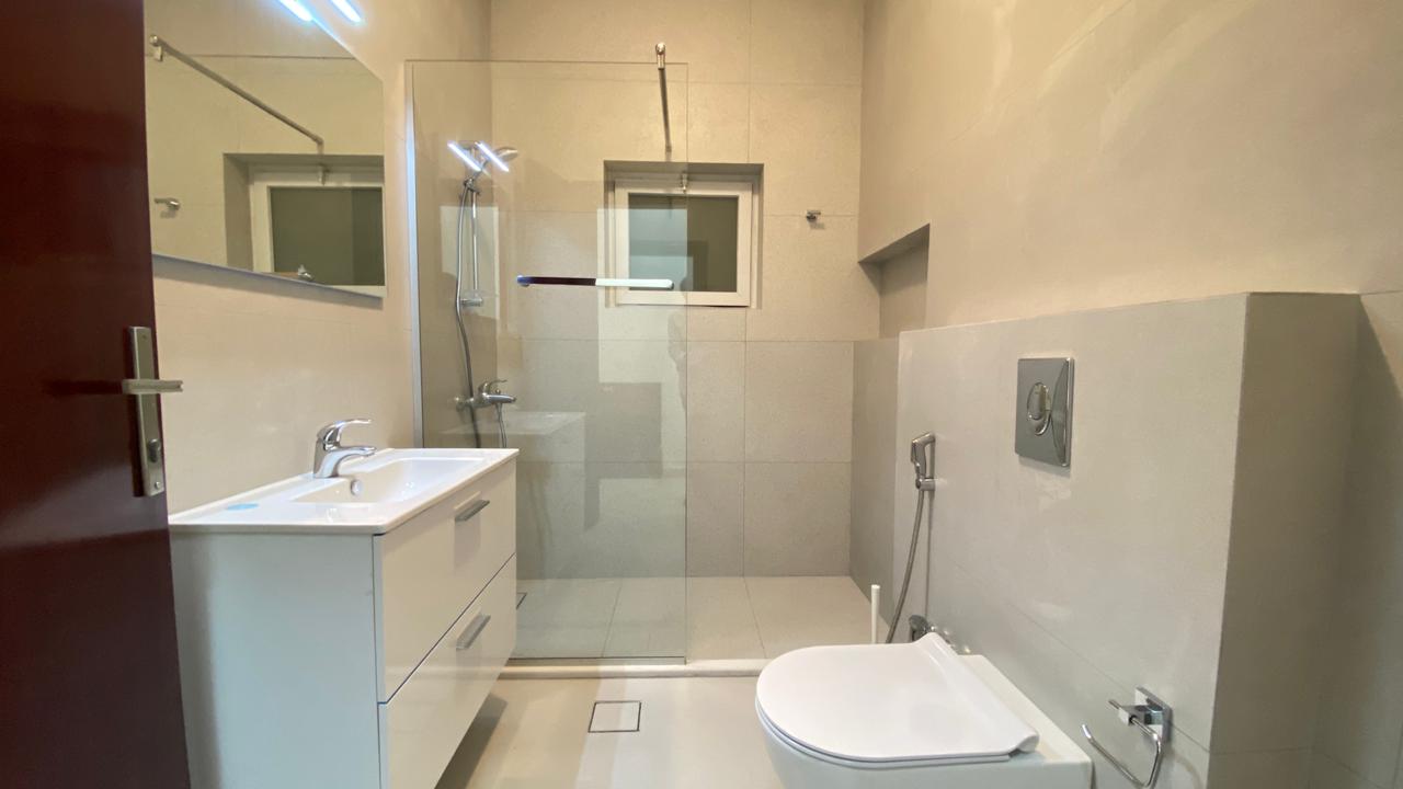 d8d776d6-3830-49c2-b9ed-fe67a81f4178 Modern bathroom with a glass-walled shower, white vanity, and wall-mounted toilet on light tiles
