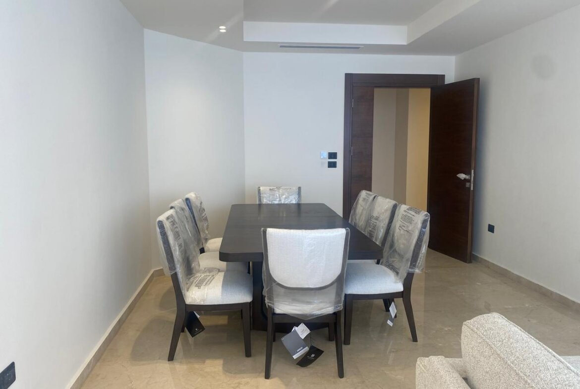 Modern dining room with a dark wooden table and six upholstered chairs still wrapped in protective plastic.