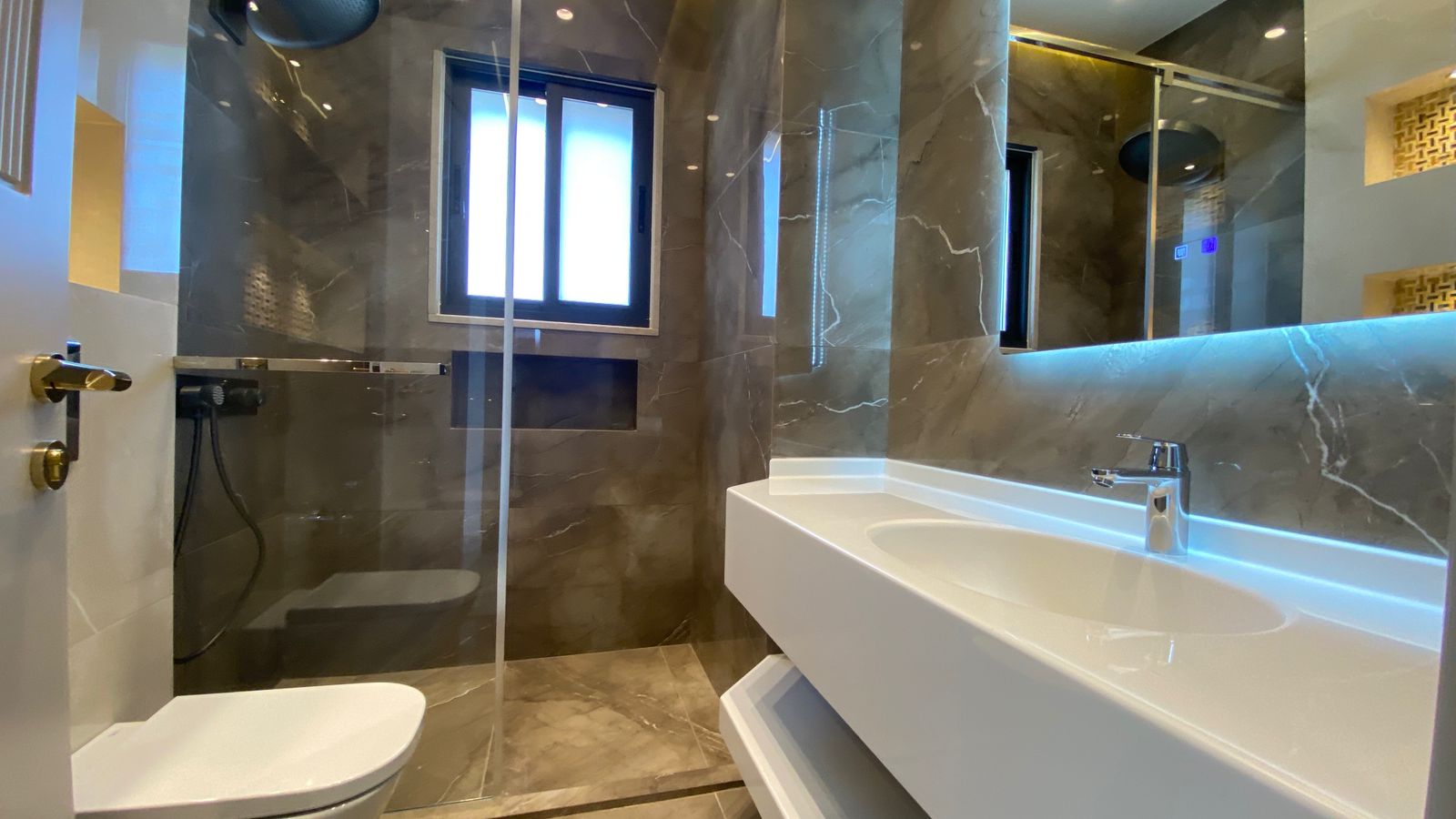 dddc9945-d969-4982-95af-225e35cd279f Modern bathroom with a glass shower enclosure, wall marble tiles, and a white sink with blue-lit LED mirror strip behind it