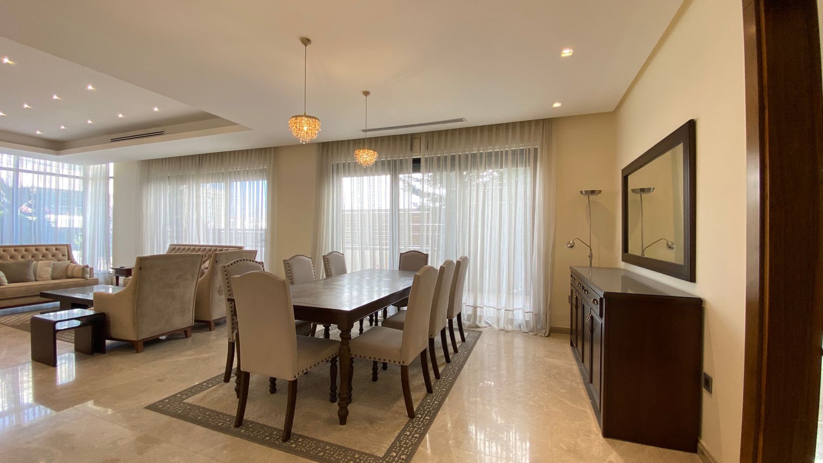dfab1ef3-6b30-43c3-9f6d-2dcfa60cf91e Elegant dining area with a dark wood table and cream upholstered chairs beneath crystal pendant lights and sheer window Drapes.