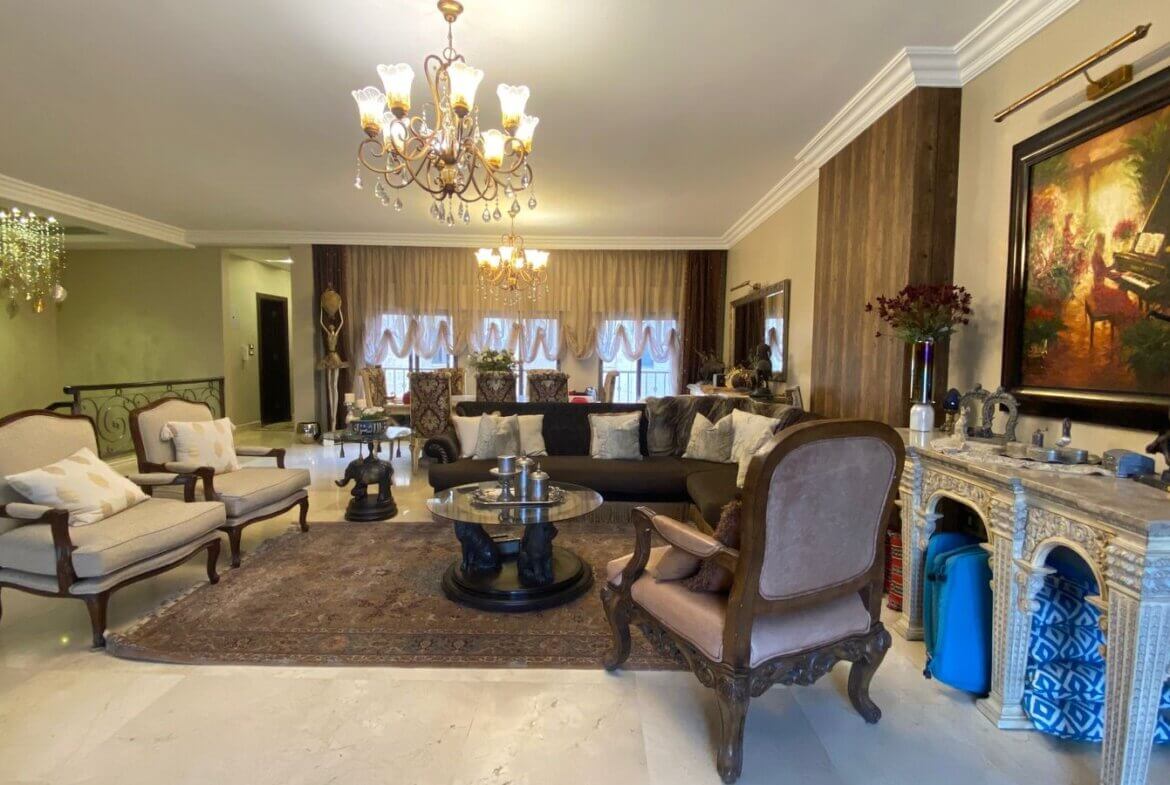 e045f007-e996-43e3-ac9b-e6cc9308d9fb Luxurious living room with ornate wooden furniture, two beige armchairs, a dark sofa, and a glass coffee table on a Persian rug.