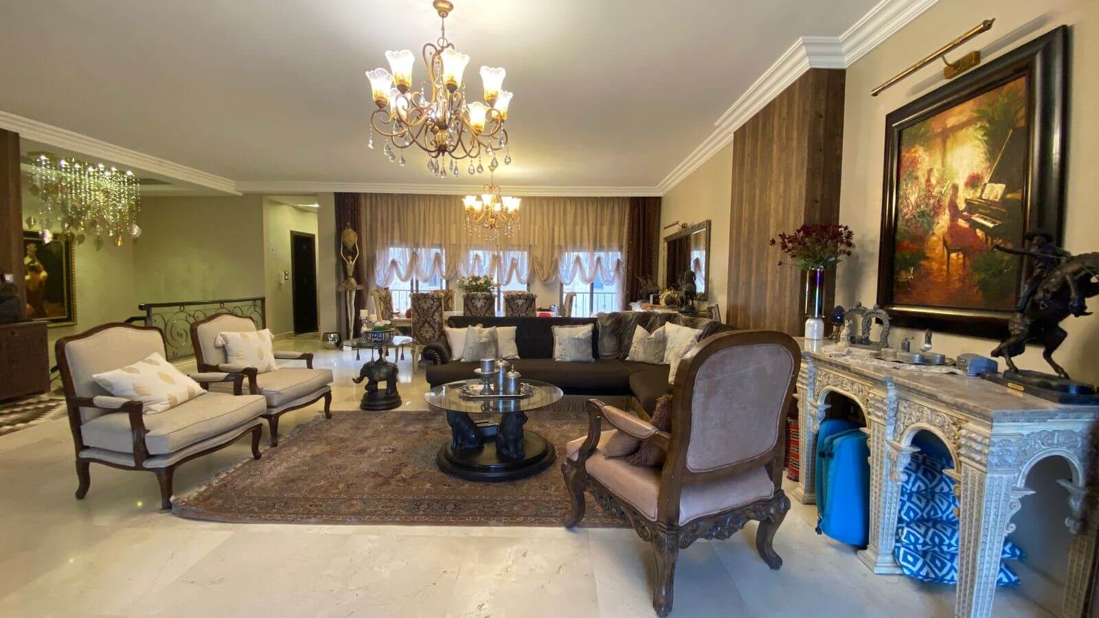 e045f007-e996-43e3-ac9b-e6cc9308d9fb Luxurious living room with ornate wooden furniture, two beige armchairs, a dark sofa, and a glass coffee table on a Persian rug.