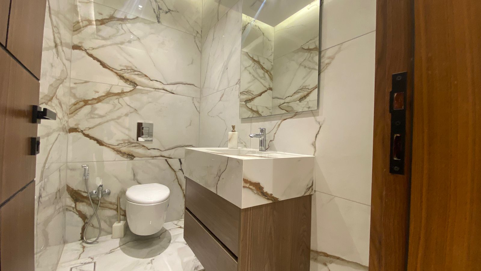 e1dd6849-0e32-4974-adb1-f9e535128c6e Modern marble bathroom with a wooden vanity, wall-mounted sink, mirror, and wall-hung toilet.