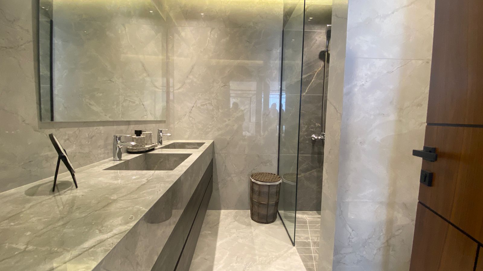 e41a2155-7e0e-4b0d-bec8-c635d8e7f9a7 Luxurious marble bathroom with a long double sink vanity, chrome faucets, and a glass-enclosed shower.