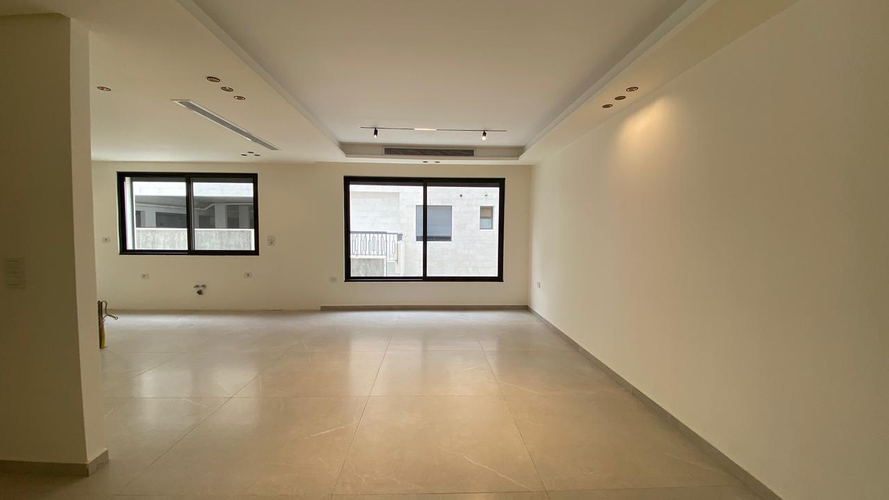 e7fddecd-c8ed-47fe-a663-9a1be80c2dc6 Spacious empty living room with two large windows, white walls, and light gray tiled floor.