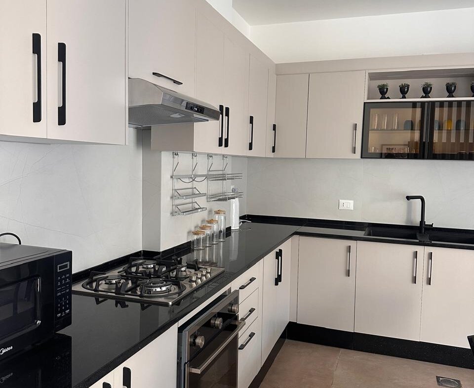 Modern kitchen with white cabinets, black countertops, and stainless steel stove and oven layout along an L-shaped wall.