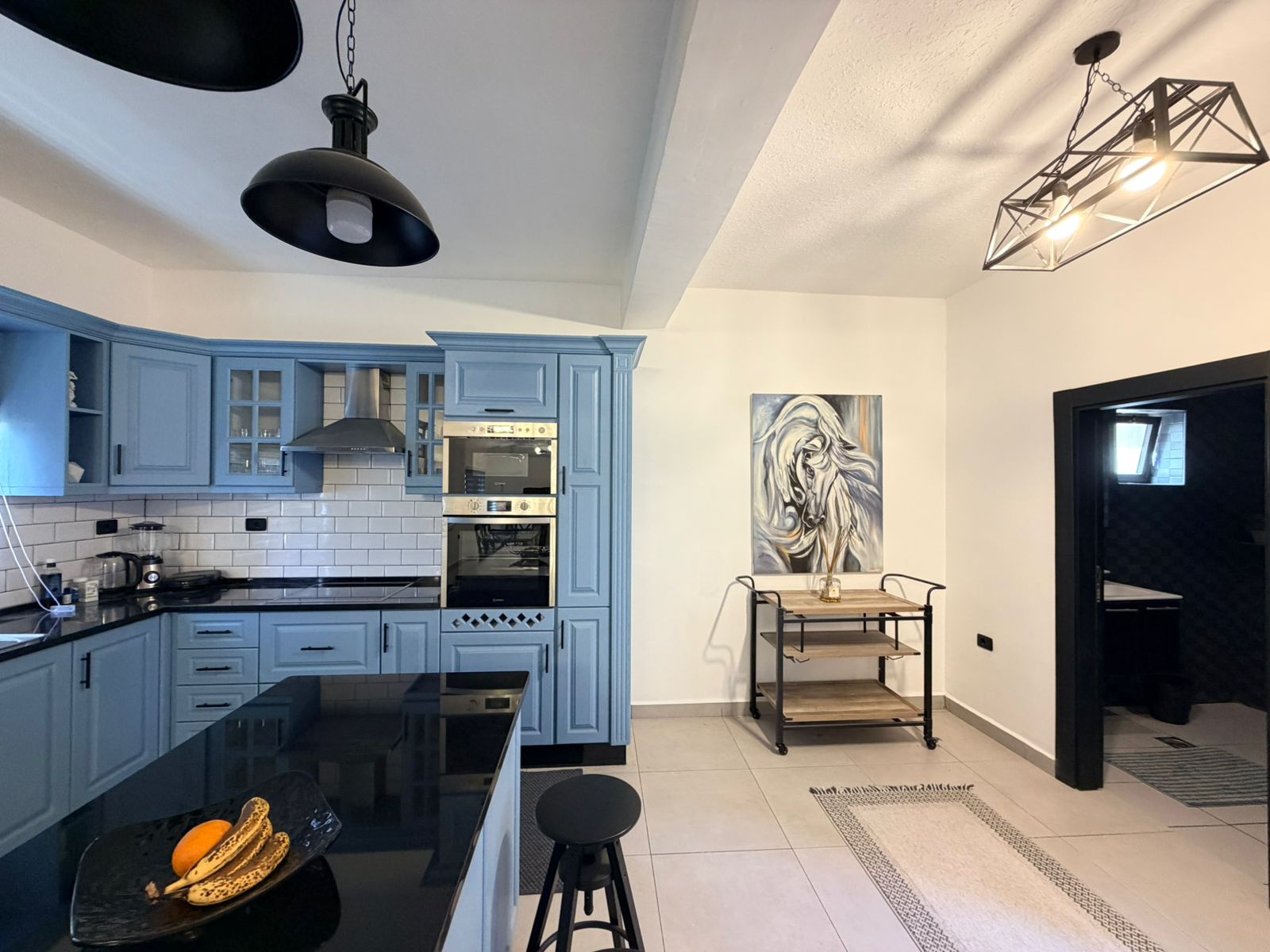 eb8c1e1f-4cbd-4ae1-a2d5-bd523a08a934 Modern kitchen with light blue cabinets, white subway tile backsplash, and stainless steel appliances. The black island countertop is in the foreground.