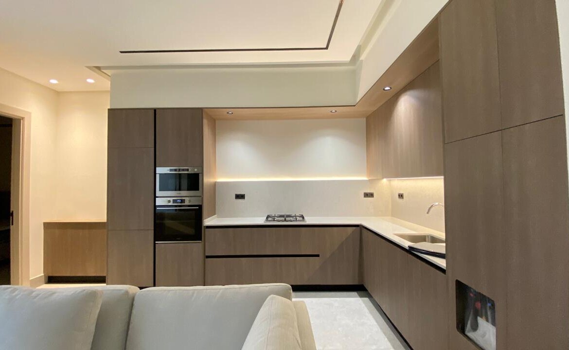 Contemporary L-shaped kitchen with dark wood cabinetry, built-in oven/microwave, white countertops, and under-cabinet lighting.