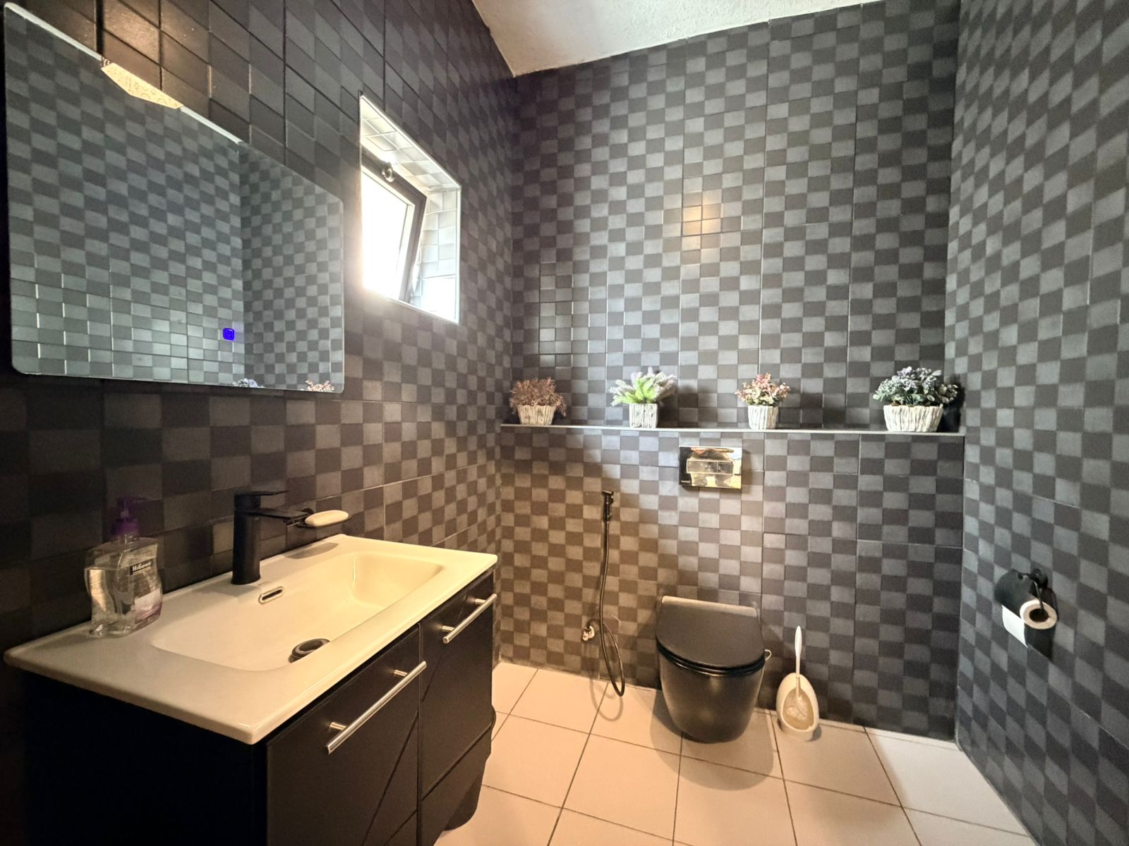 f44bd126-f355-49af-b2c0-ab243b355a38 Modern bathroom with dark gray checkered walls, white sink, black faucet, and dark vanity under a large mirror.