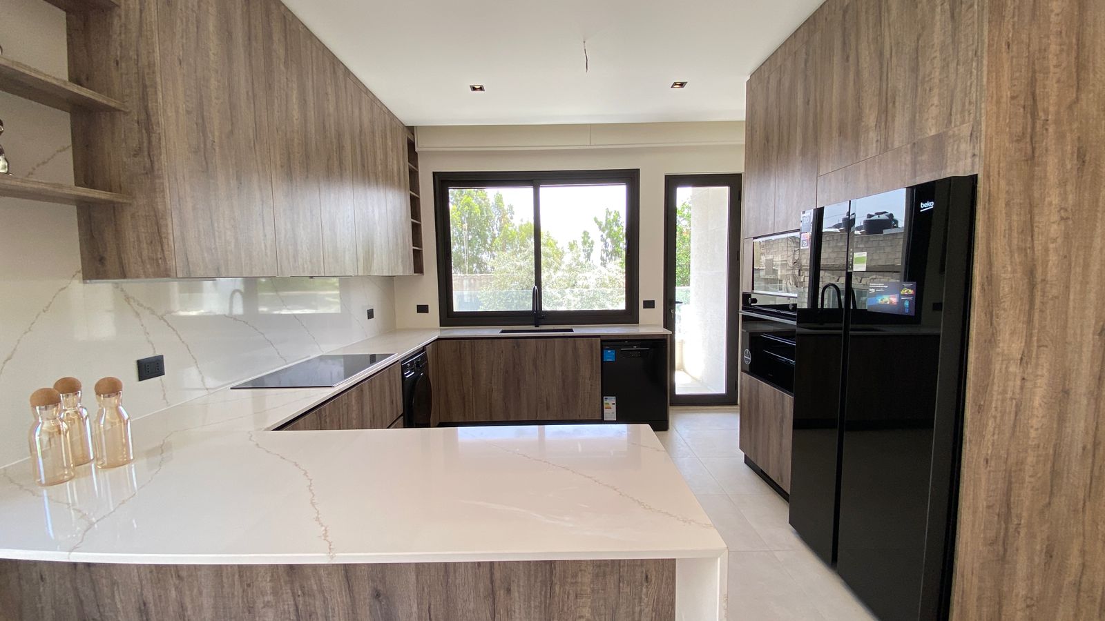 f739b0c9-7693-4fcc-8462-40c439b3fc14 Modern kitchen with wood grain cabinets, white marble countertops, and a large window over the sink.