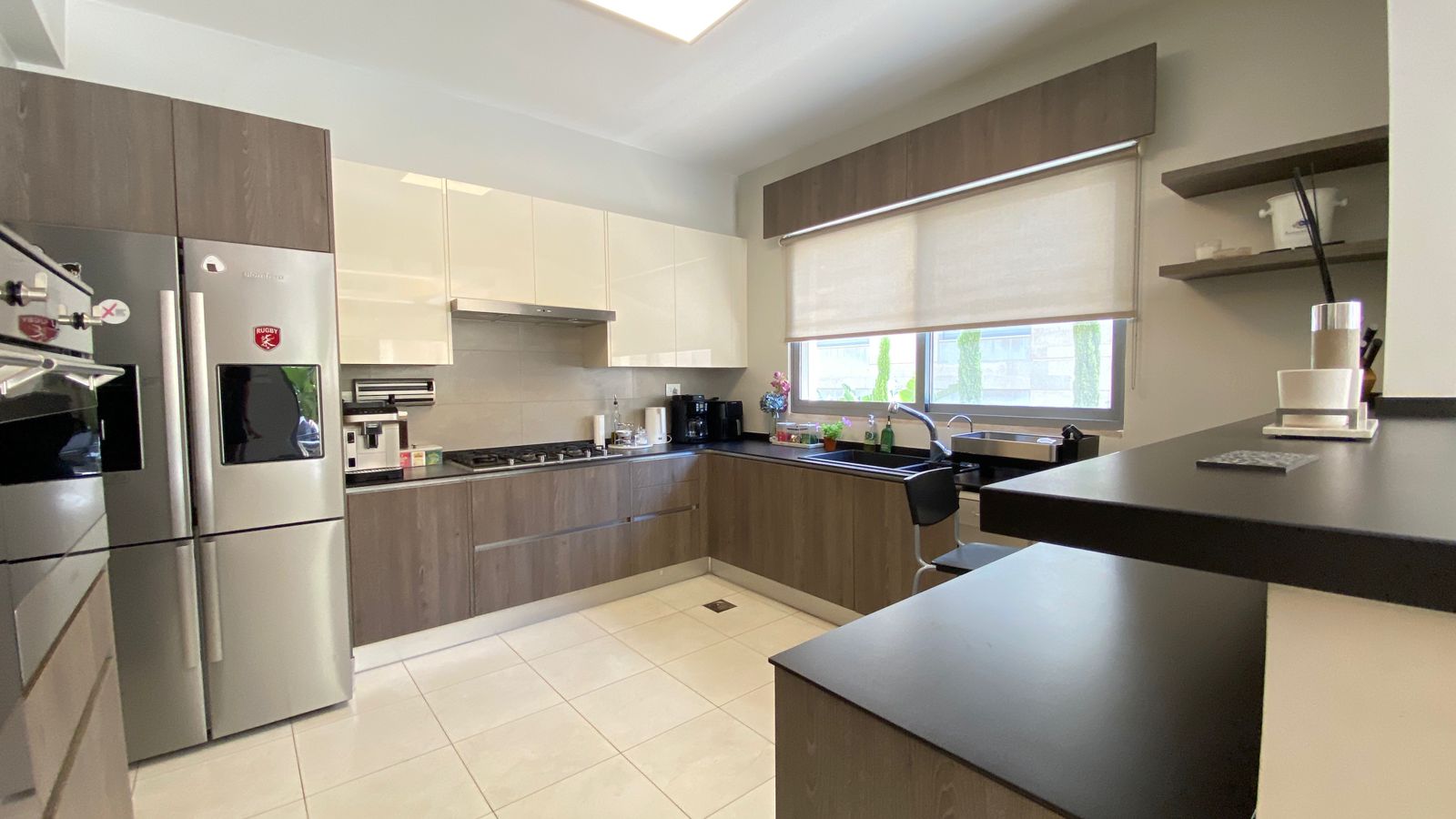 fa0ab2fe-bb90-4a33-9340-89270a734fb7 Modern L-shaped kitchen with brown lower cabinets, white upper cabinets, stainless steel French-door fridge, and a large window over the sink. (Informative)