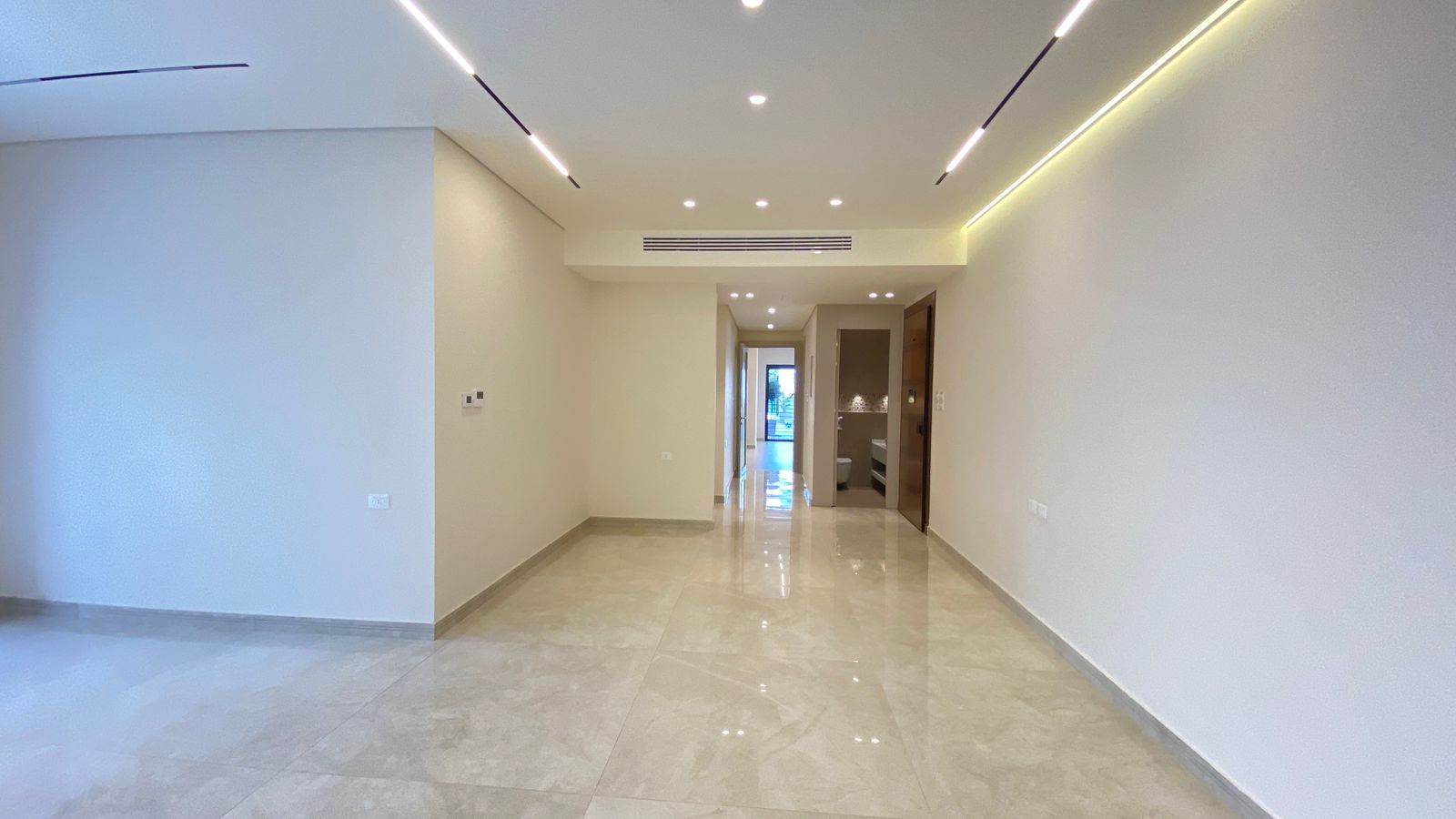 fa8f96ec-fca2-4bcf-ae80-8890d6fd99a8 Bright, minimalist hallway with light-colored walls, glossy tile floor, and linear ceiling lights leading to a doorway at the far end of the space.