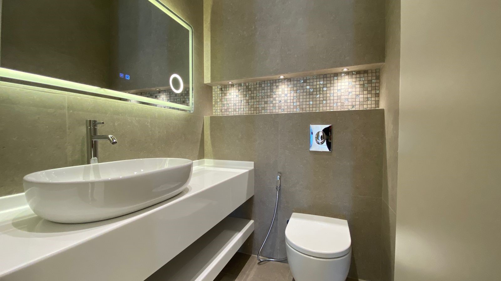 fcec466c-1c95-4790-8bf7-d4318daea560 Modern bathroom with a white oval vessel sink on a white counter, wall-mounted faucet, and backlit mirror.