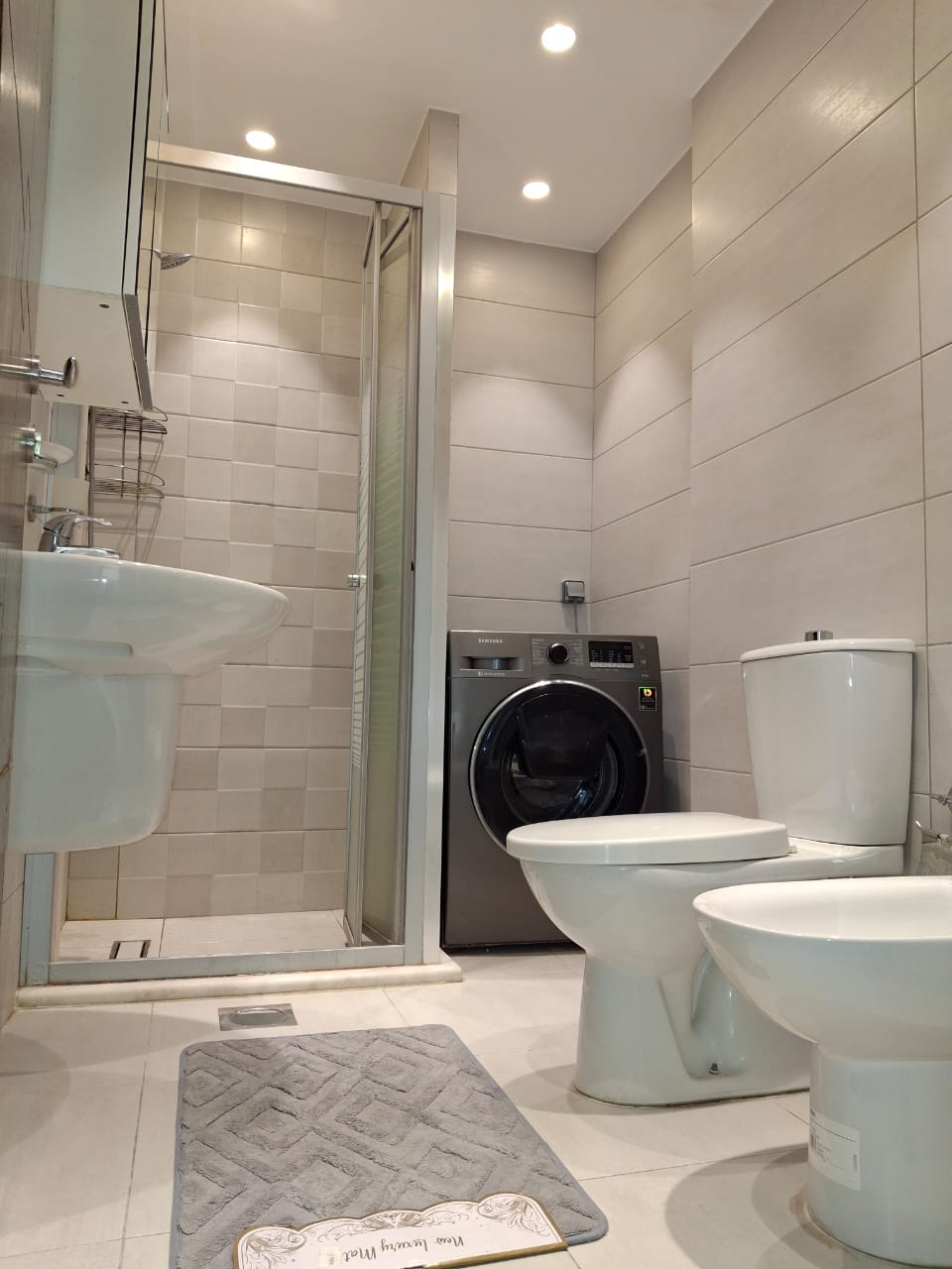 03e23346-ce71-4a48-b6df-52bc634f6e45 Modern bathroom with shower enclosure, front-loading washing machine, toilet, and bidet in a compact space.