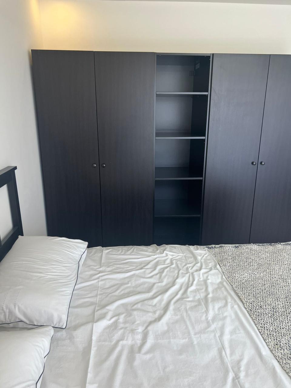 047330a5-70c4-449b-bff3-814eadb4dd38 Dark wooden wardrobe with one open middle section showing shelves, flanked by closed doors, in a bedroom with a bed in front.