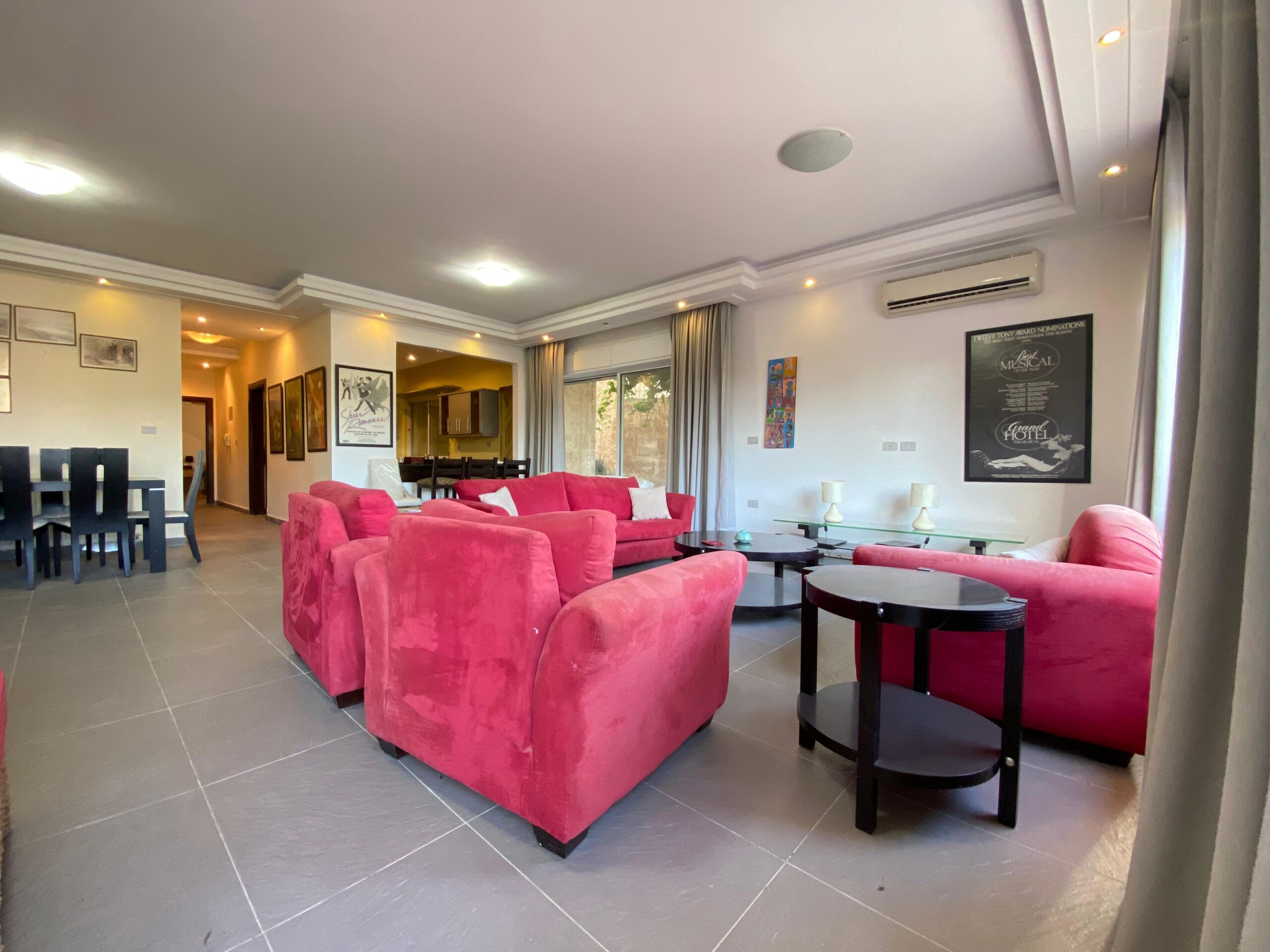 06ccb3e6-e570-4d11-ba9b-d48976848447 Bright living room with vivid pink sofas and dark wood coffee tables, framed art on the walls, and large windows with grey curtains.