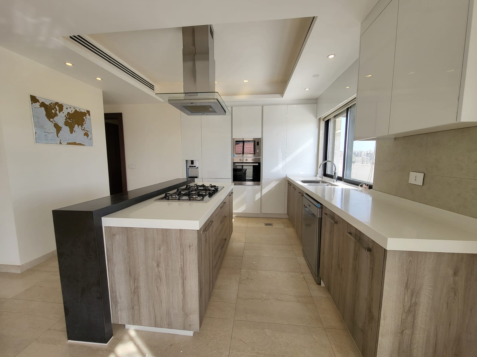 0b2c11c6-09fb-448f-b51b-f51cbd2b9309 Modern L-shaped kitchen with island gas stove, stainless range hood, white cabinets, and a sink by a large window.