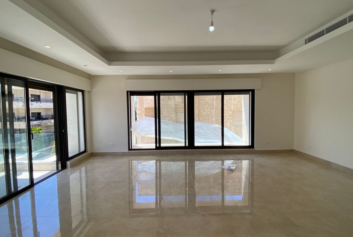 Bright empty living room with glossy beige tile floor and large sliding glass doors opening to a balcony.Parsed reflections on the floor and a minimalist ceiling with recessed lighting reveal a modern, open space.