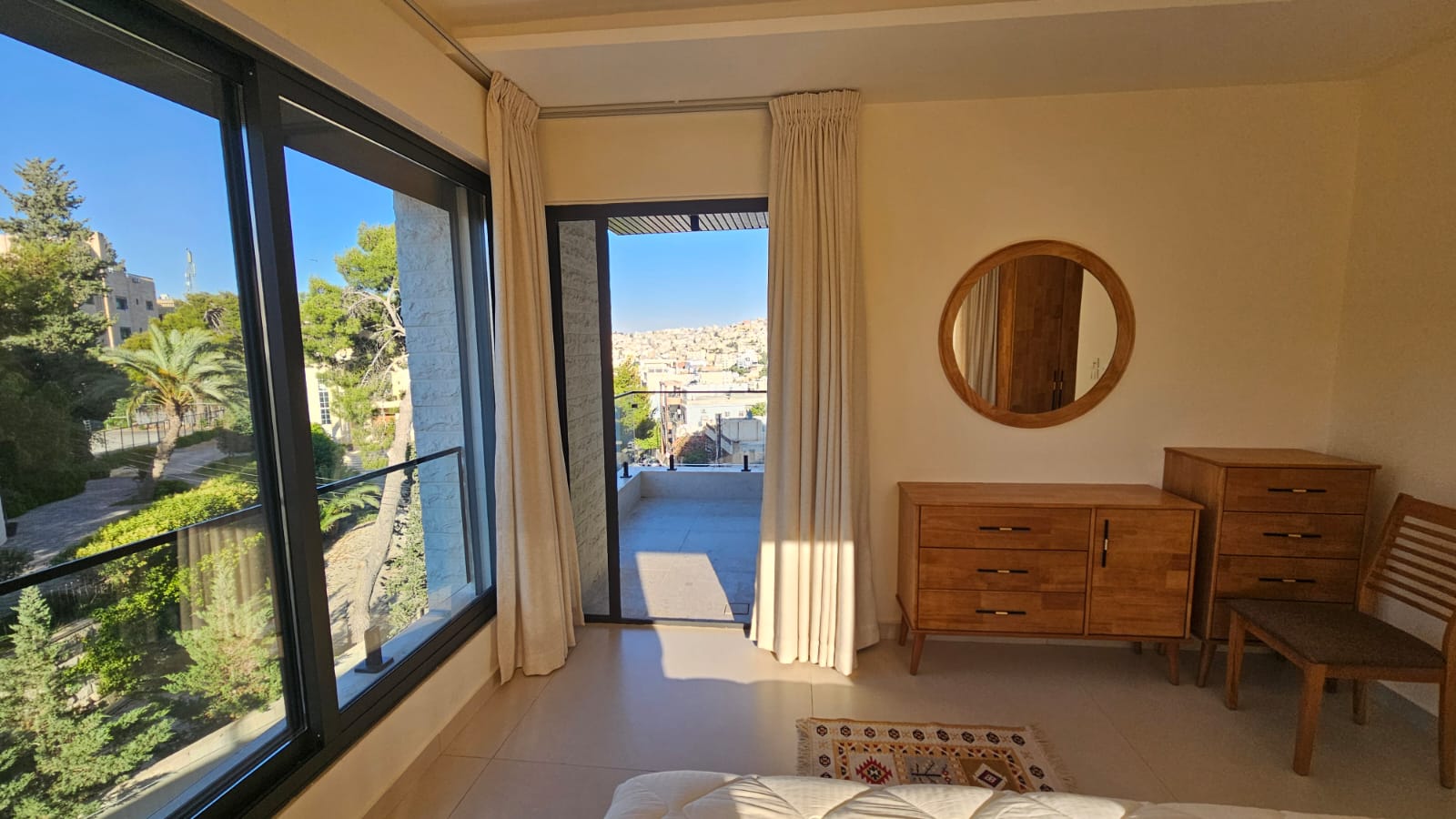 122cffd0-de77-4b9a-b641-a4534ff72fcb Bright bedroom with large sliding glass doors to a balcony, beige curtains, and a city view outside.