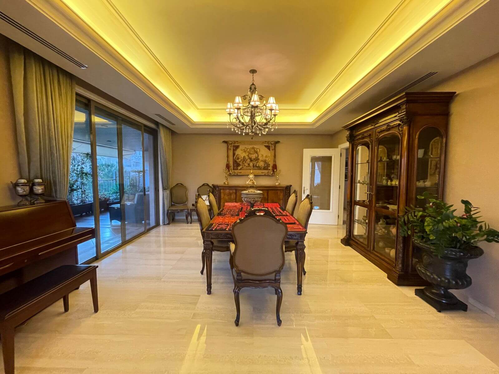 140235d3-56e1-4dde-a9ea-4072b26e227e Elegant dining room with a dark wood table and six chairs, ornate chandelier overhead, and a glass-front cabinet nearby.