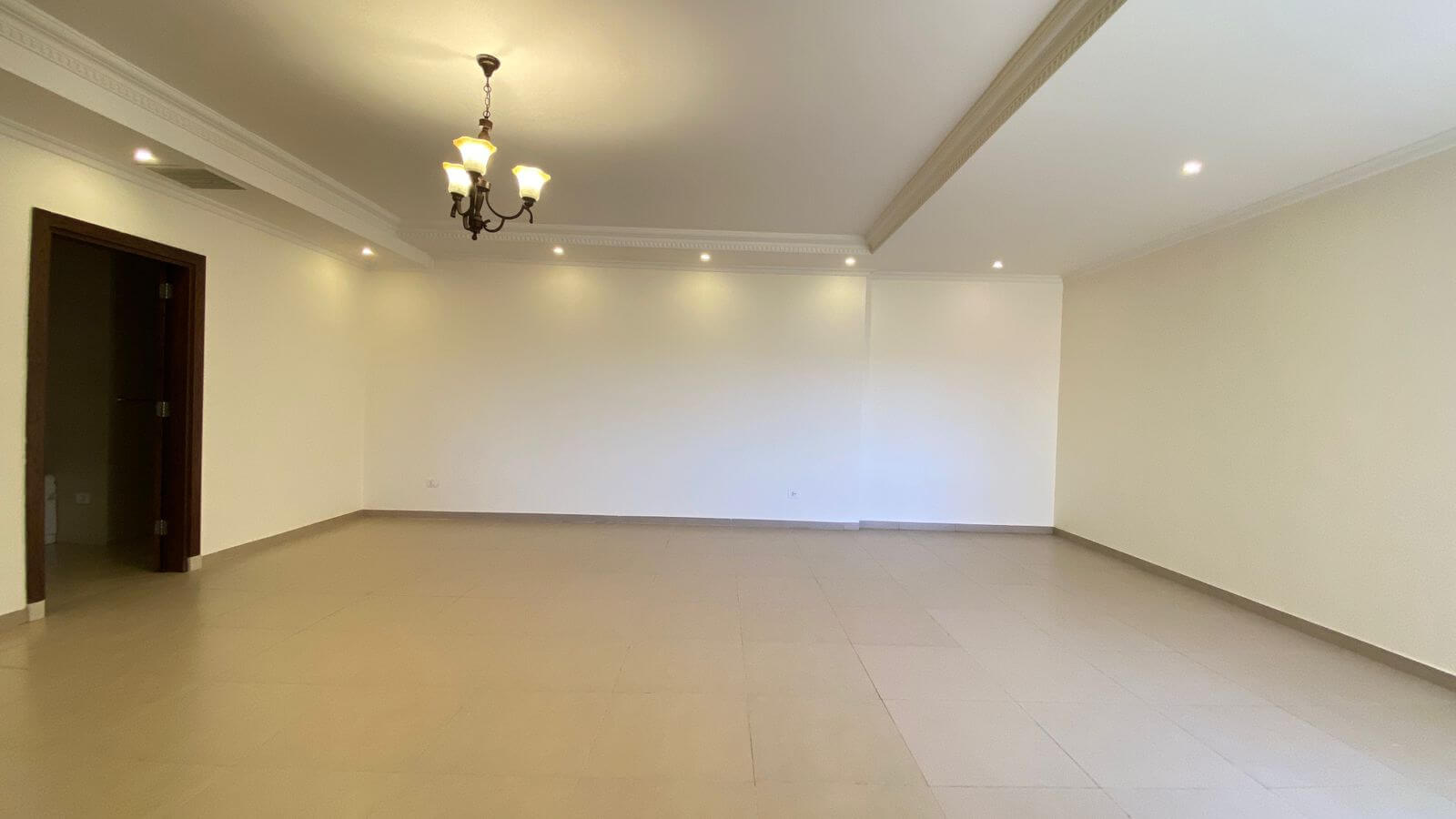 14d46f91-ab4f-4371-9177-831bd3c5b06e Empty, spacious living room with beige tile floor, cream walls, crown molding, and a hanging chandelier as focal point.