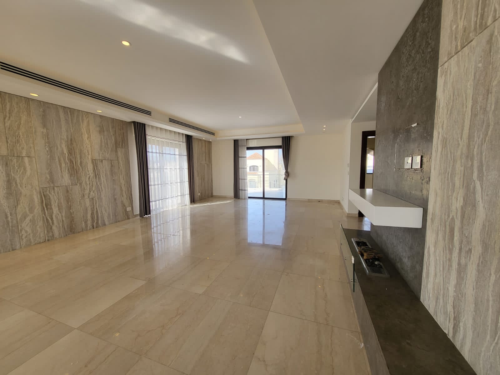 1547cc1d-f27a-42fd-8ce1-e28b6fe0e3de Bright, empty living room with marble floors, stone accent wall, and a built-in fireplace overlooking a balcony through glass doors