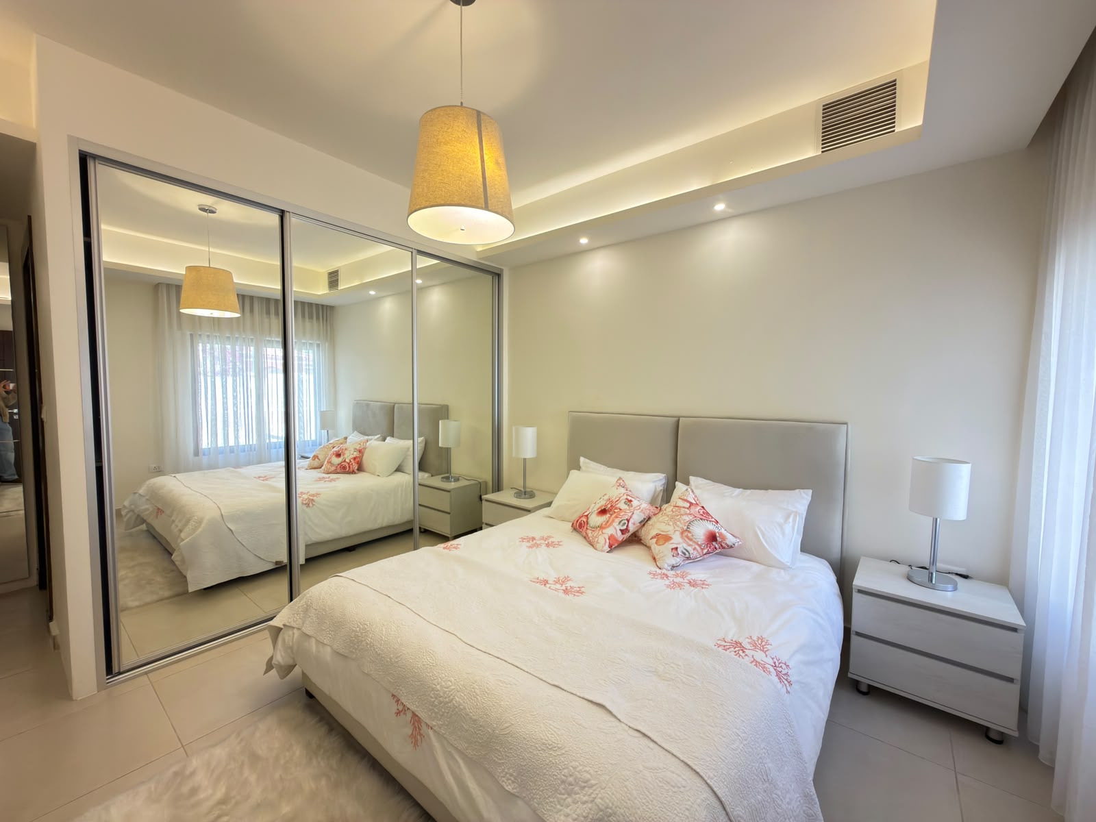 162aa3dd-a5cc-4c41-b08e-1dc22991bb32 Modern bedroom with a large bed, beige headboard, and mirrored sliding wardrobe reflectively opening the space.