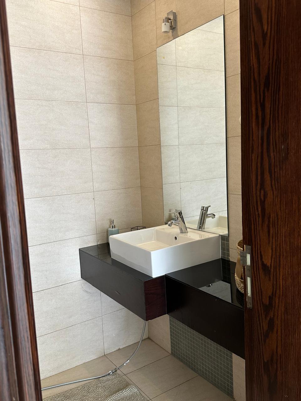 18e89c41-5525-410a-82cf-783f7fbf1293 Modern bathroom vanity with a square white sink on a dark floating countertop, tall mirror and beige tiled walls.