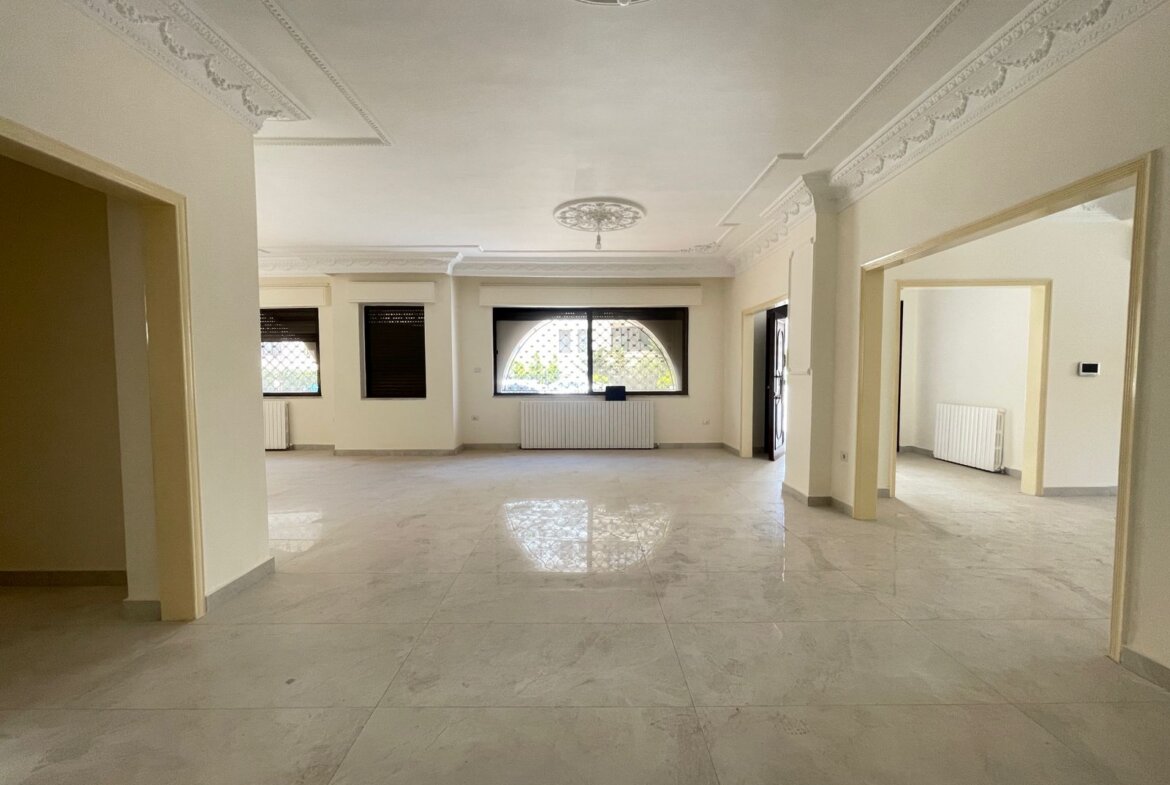 Spacious empty room with decorative ceiling molding, arched window, and radiators along the wall.