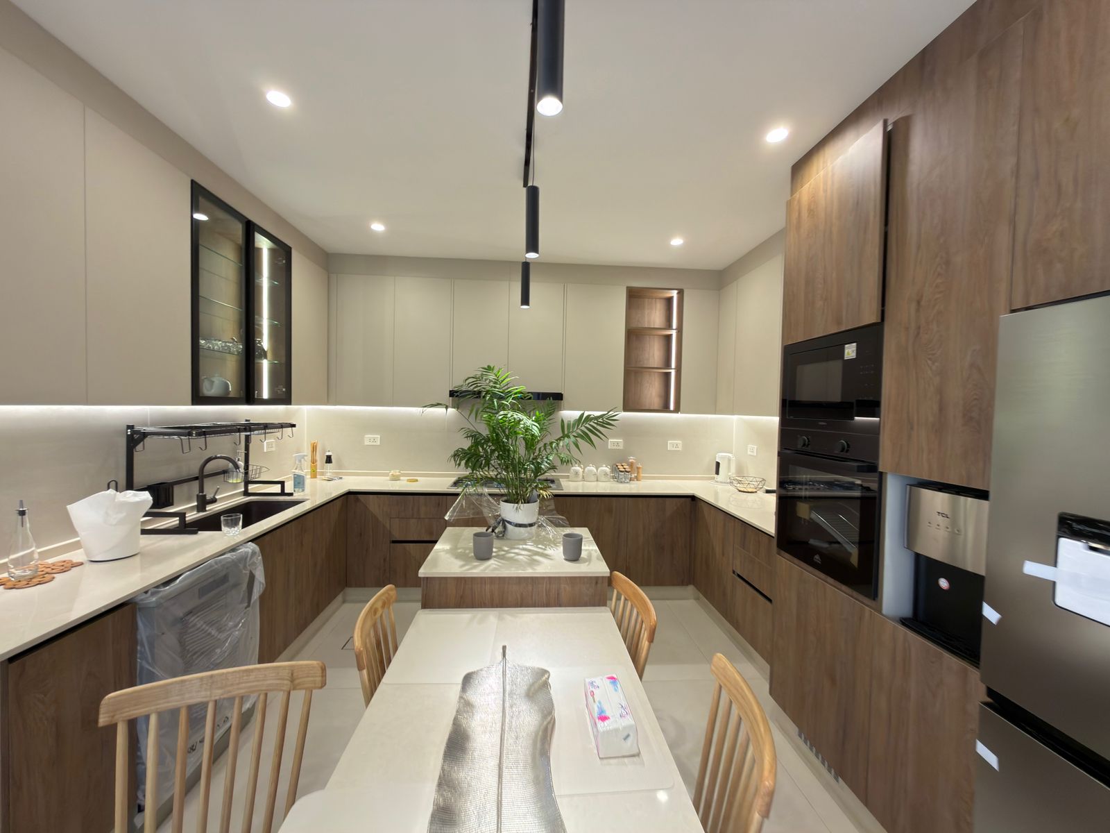 22cb40a1-4598-45e5-979a-eb076c0714d2 Modern U‑shaped kitchen with wooden lower cabinets, light gray upper cabinets, and a central island with a plant centerpiece.